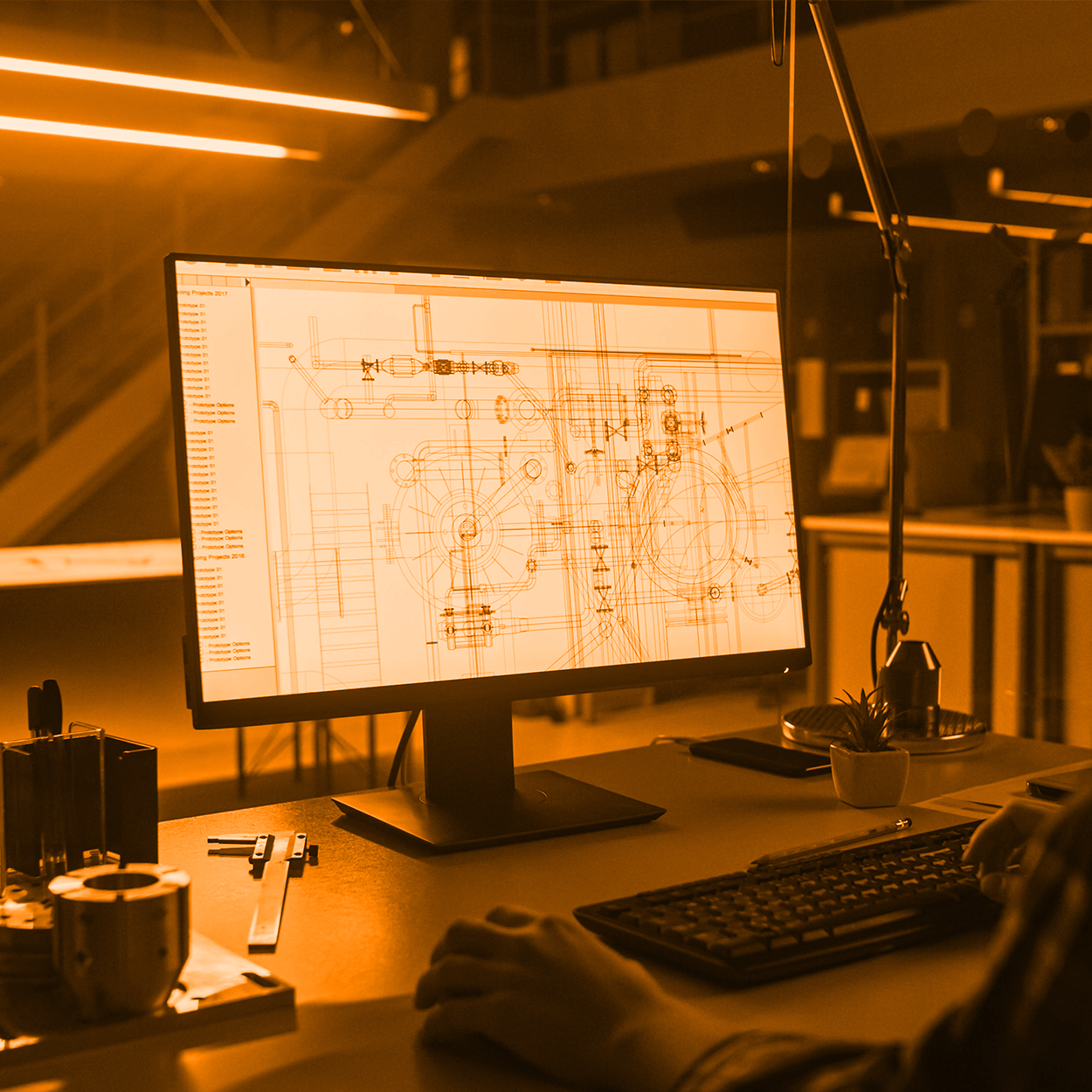 Engineer working at a desk with a computer monitor displaying technical schematics and diagrams, illuminated in an orange hue.